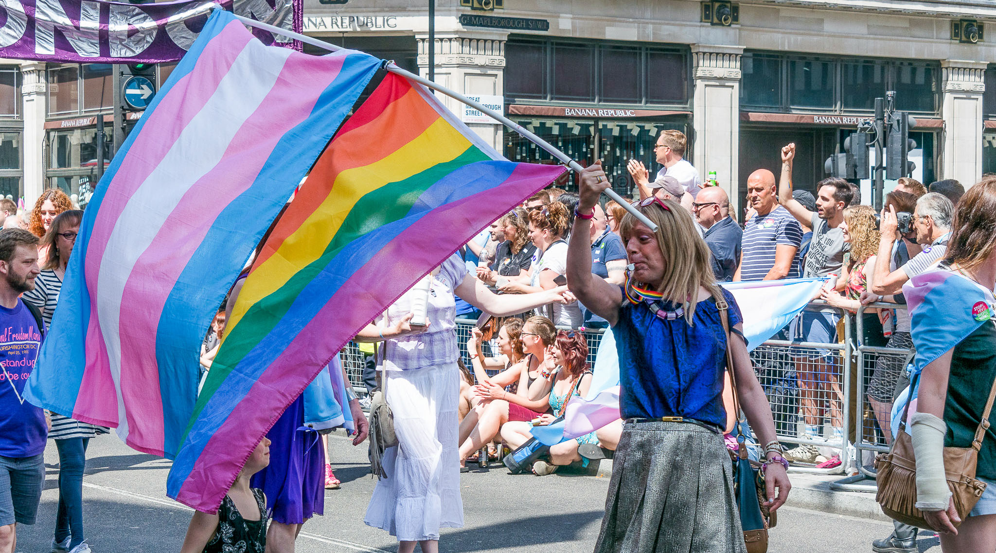 A person holds trans and rainbow flags at a Pride march
