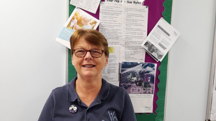 Sue Ryles smiles in front of a UNISON noticeboard