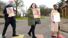 Three people holding copies of the Anti-Racism Charter walk over a rainbow zebra crossing outside Hellesdon Hospital